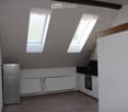 Modern kitchen with wooden flooring, white walls, stainless steel refrigerator, built-in oven, and radiator under the windows.