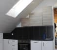 Modern kitchen with white cabinets, black countertops, and a built-in oven. Features a skylight window and sleek design.