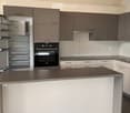 Modern kitchen with grey and white cabinets, stainless steel appliances, island countertop, and open refrigerator.