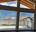 Bright, spacious balcony with large glass doors opening to a scenic mountain view. The balcony features a modern metal railing and tiled flooring.