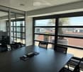 Modern office space with large windows, black conference table, chairs, laptop, and office equipment.