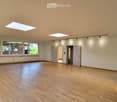 Empty room with wooden flooring, large windows, and skylights, featuring white walls and recessed lighting.