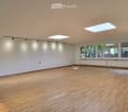 Empty room with wooden flooring, white walls, large windows, and skylights.