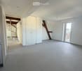 Empty room with tiled floor, white walls, and a sliding glass door leading to a balcony. A white cabinet and a wooden staircase are visible in the background.
