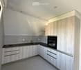 Modern kitchen with light wood cabinets, black countertops, and built-in oven. Features a sink and sleek design.