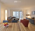 Modern living room with a sectional sofa, coffee table, dining table, chairs, and a balcony view. The room features wooden flooring, large windows, and contemporary decor including a lamp and a cabinet.