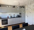 Modern kitchen with grey cabinets, black countertop, stainless steel sink, built-in oven, and a black dining table with chairs.