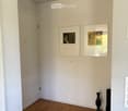 Empty hallway with wooden flooring, white walls, two picture frames, and two vases.