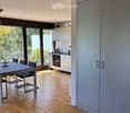 Modern dining area with a sleek black dining table and chairs, adjacent to a contemporary kitchen with white cabinets and stainless steel appliances.
