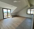 Empty attic room with wooden flooring, large windows, and a view of the cityscape.