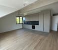 Modern kitchen with light wood flooring, white cabinets, and a black countertop. Features a sink, faucet, and built-in oven.