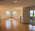 Empty room with wooden flooring, large windows offering a scenic view, and a sliding glass door leading to a balcony.