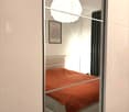 Modern bedroom with a single bed, orange blanket, a hanging spherical lamp, and a picture frame on the wall.