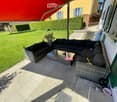 Balcony with a black wicker sofa and coffee table, overlooking a well-maintained lawn and garden.