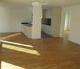 open plan kitchen and living room, hardwood floors, white walls, island with sink and faucet, glass sliding doors