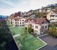 Aerial view of a residential area with multiple houses, green spaces, and a winding road.