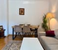 A modern living room with a sofa, coffee table, dining table, chairs, a floor lamp, a plant, a clock, and a picture frame on the wall.