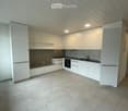 Modern, minimalist kitchen with white cabinets, a built-in refrigerator, oven, and sink. The space features a clean, contemporary design with a tiled floor and recessed lighting.