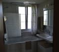 Bathroom with a bathtub, sink, mirror, and towels. Features a window with blinds and a floral curtain.