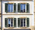 Classic European-style building with green shutters, arched entrance, and small outdoor seating area.