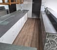 Modern kitchen with white cabinets, dark countertops, and a wooden floor. Features a sink with a faucet and built-in cabinets.