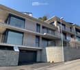 Modern multi-story building with balconies, large windows, and a stone facade. Features include a garage and a raised ground floor.