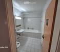 Clean, tiled bathroom with a white sink, bathtub, mirror, and toilet. The walls are tiled with a decorative border, and the floor is covered in white tiles.