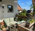 Balcony with a small couch, wooden chair, green table, and potted plants