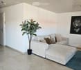 Modern living room with a white sectional sofa, ottoman, decorative pillows, a potted plant, and artwork on the wall.
