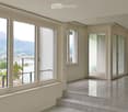 Empty room with large windows offering a scenic mountain and lake view, polished tile floor, and a small step leading to a balcony area.