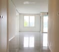 Empty hallway with white walls, polished tile floors, and recessed lighting. Features a window and a glass door leading to an outdoor area.
