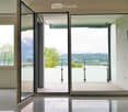 Open hallway with large glass doors leading to a balcony, offering a scenic mountain view and greenery.