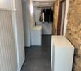Narrow hallway with white walls, dark tiled floor, built-in coat rack, and small white console tables on both sides.