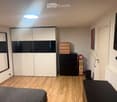 Modern bedroom with a grey bed, white wardrobe, black dresser, mirror, small table, and mounted TV.