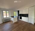 Modern kitchen with white cabinets, black countertop, and wooden flooring. Features an island with a black countertop and a built-in oven.