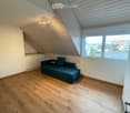 Attic room with wooden flooring, slanted wooden ceiling, large window offering a view, and a blue sofa.