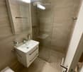Modern bathroom with beige tiles, a white sink with a chrome faucet, a large mirror, a glass-enclosed shower, and a toilet.