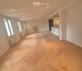 empty room, wooden parquet floor, white walls, white radiators, windows, kitchen area