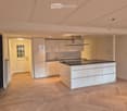 modern kitchen, white cabinets, black countertop, island, wooden floor, white walls, ceiling lights, exhaust hood, sink, faucet