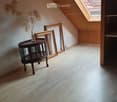 Attic room with wooden floors, slanted wooden ceiling, and skylight. Features a small round table with a vase and two large picture frames leaning against the wall.