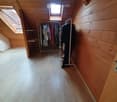 Attic room with wooden walls and floor, skylight windows, clothing rack with hanging clothes, and a small shelf.