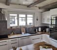 Modern kitchen with white cabinets, stainless steel appliances, wooden countertops, and a large window. Features include a sink, faucet, oven, refrigerator, and various kitchen items on the counter.