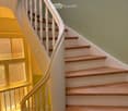 Spiral staircase with wooden steps and white balustrade, leading to an upper level. The walls are painted in a light green color, and the floor is tiled.