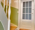 Hallway with a staircase leading upwards, green and beige walls, wooden steps, white balusters, and a frosted glass door at the end.