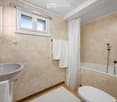 Bathroom with a sink, bathtub, toilet, and white towels. Features a window with a curtain and a small white rug on the floor.