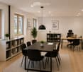 Modern office space with a large conference table, chairs, a desk with a laptop, shelves, and plants.