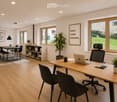 Bright, modern office space with wooden flooring, large windows, a desk with a laptop, chairs, a small table with stools, shelves, and plants.
