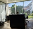 Modern office space with large windows, wooden floor, desk, office chair, screen, and printer.