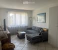 Living room with grey sectional sofa, ottoman, glass coffee table, TV, and decorative plants.