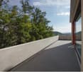 Modern balcony with a concrete railing, overlooking a lush green landscape with trees and distant hills.